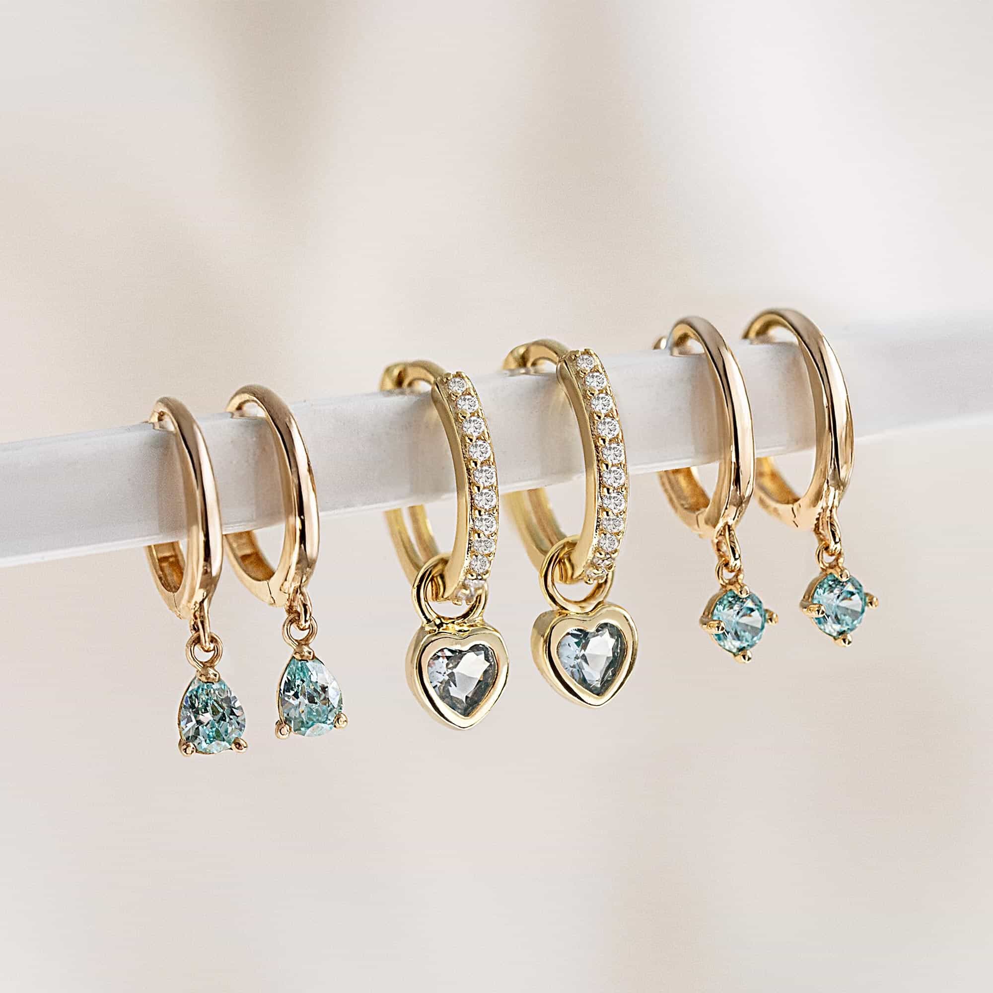 Gold huggie hoops with pavé, blue heart and round blue stone drops lined up on a bar