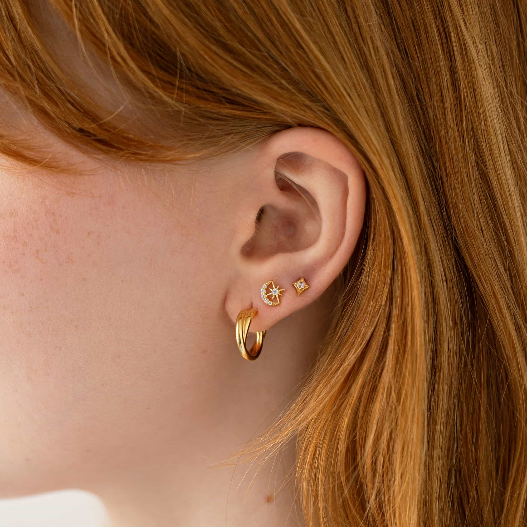 Gold celestial studs and hoops with clear stones, styled in an ear stack on a model