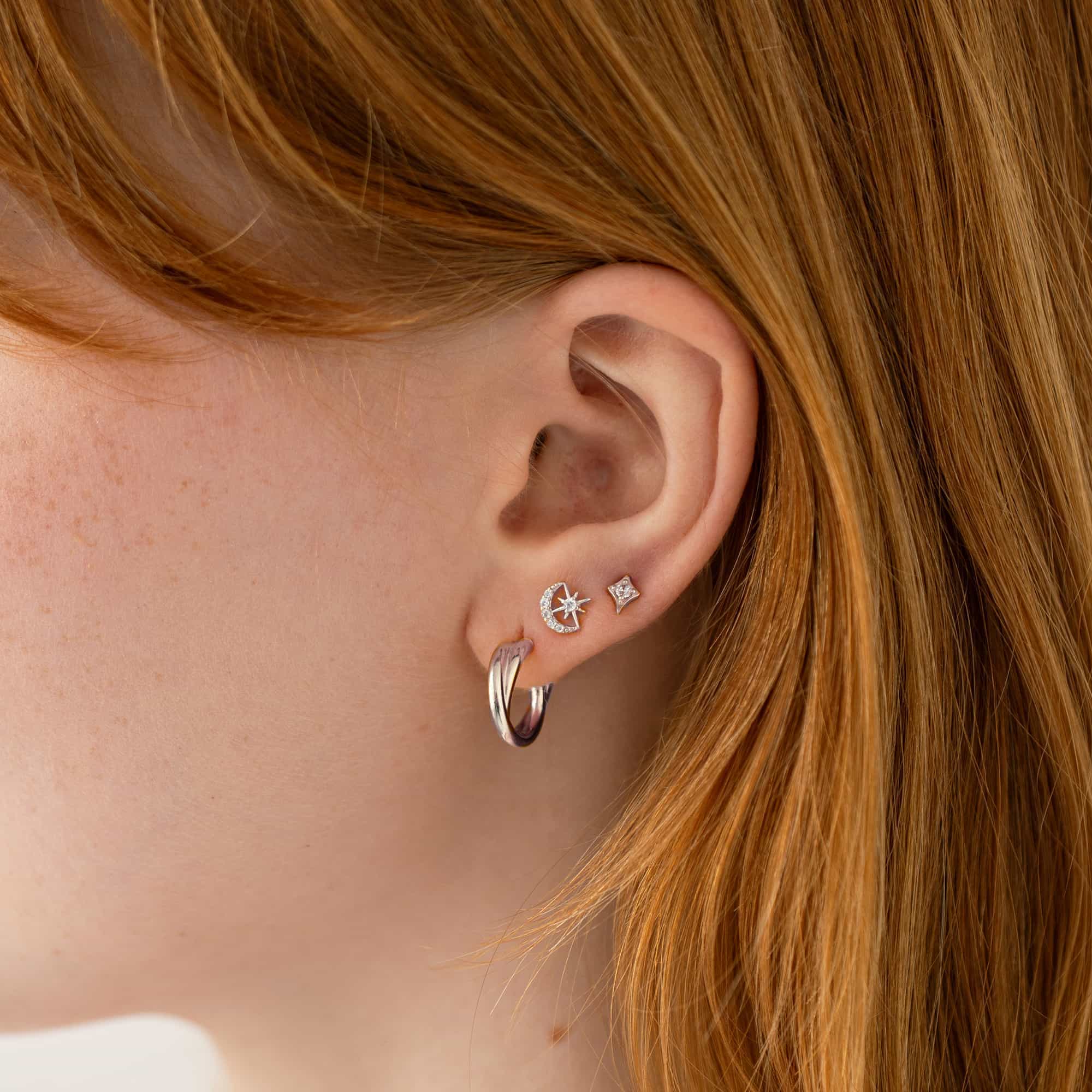 Silver celestial studs and hoops with clear stones, styled in an ear stack on a model