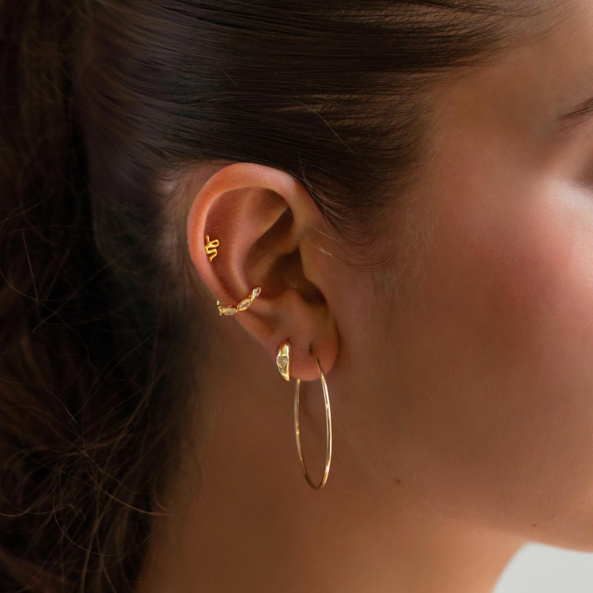 Gold vermeil serpent flat back stud shown on a model's helix, with a thin hoop on the lobe