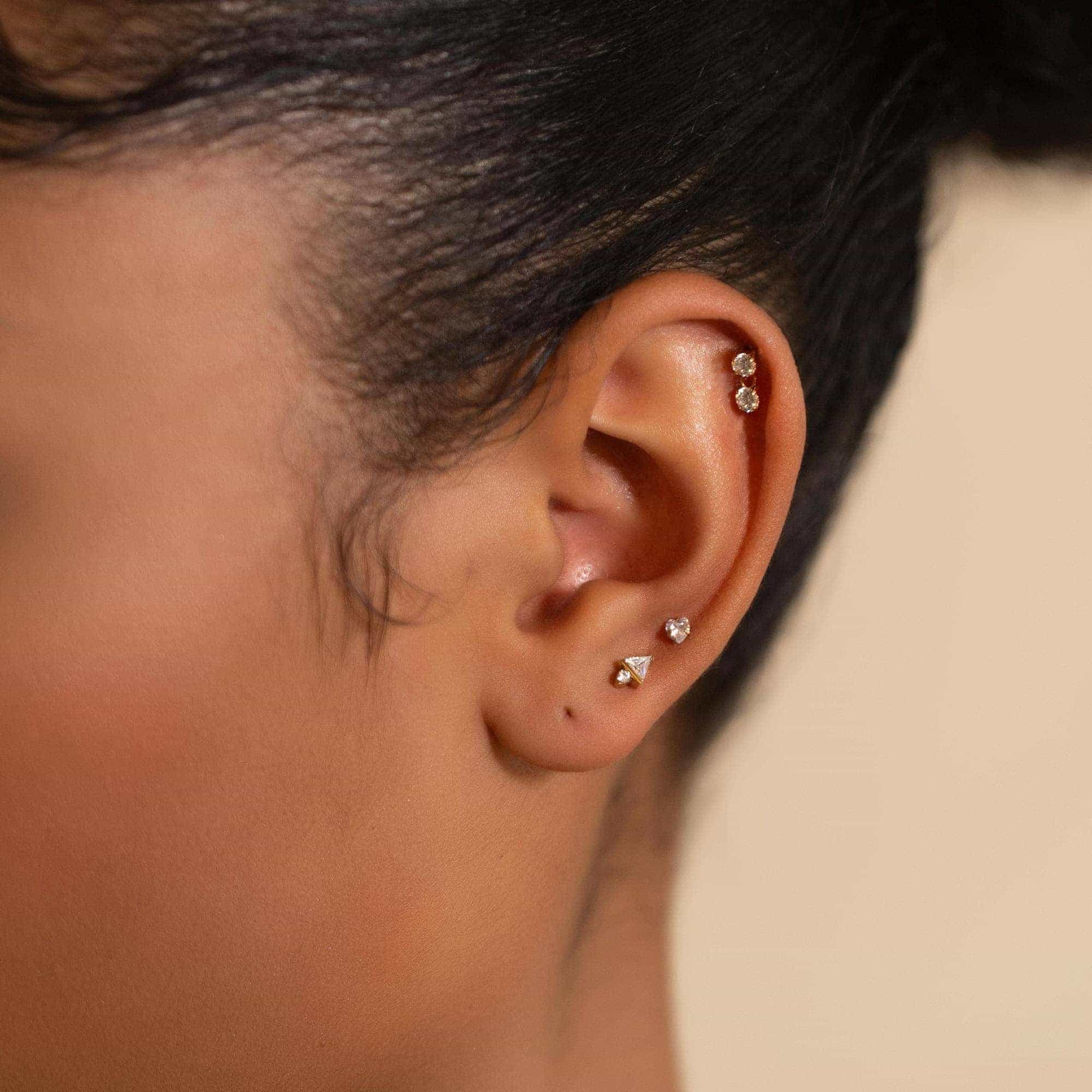 Gold flat back studs with clear stones shown on a model's lobe and helix