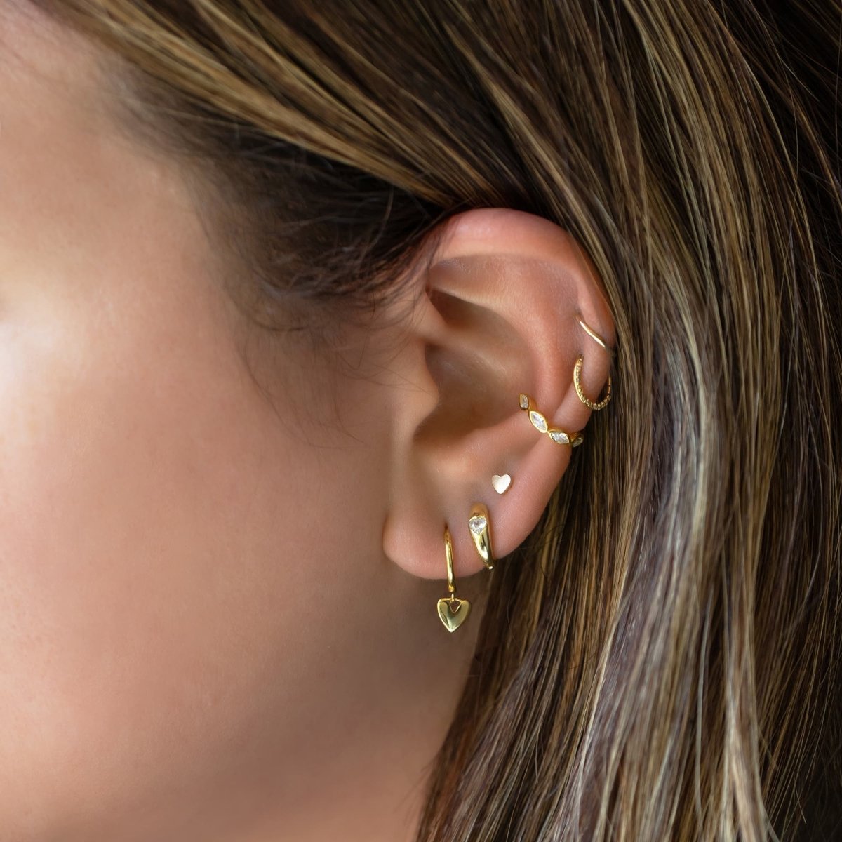 Gold vermeil heart huggie hoops styled in a gold ear stack, shown on a model's ear