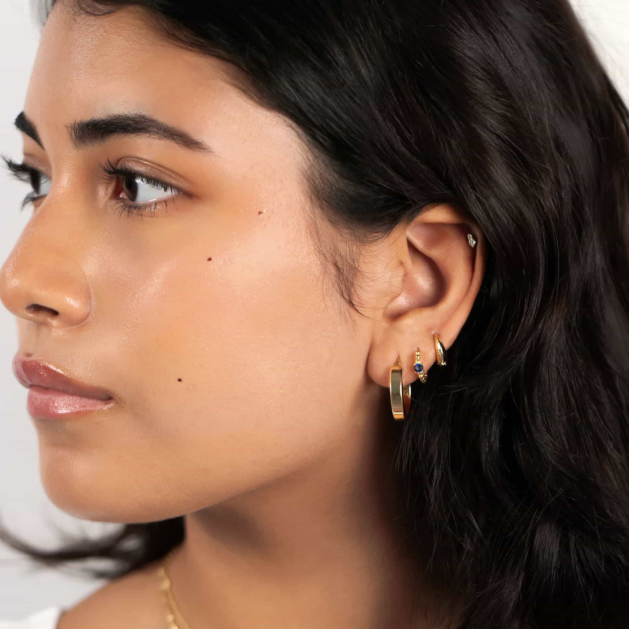 14K gold duo white zirconia flat back stud, shown on a model's lobe beside gold hoops