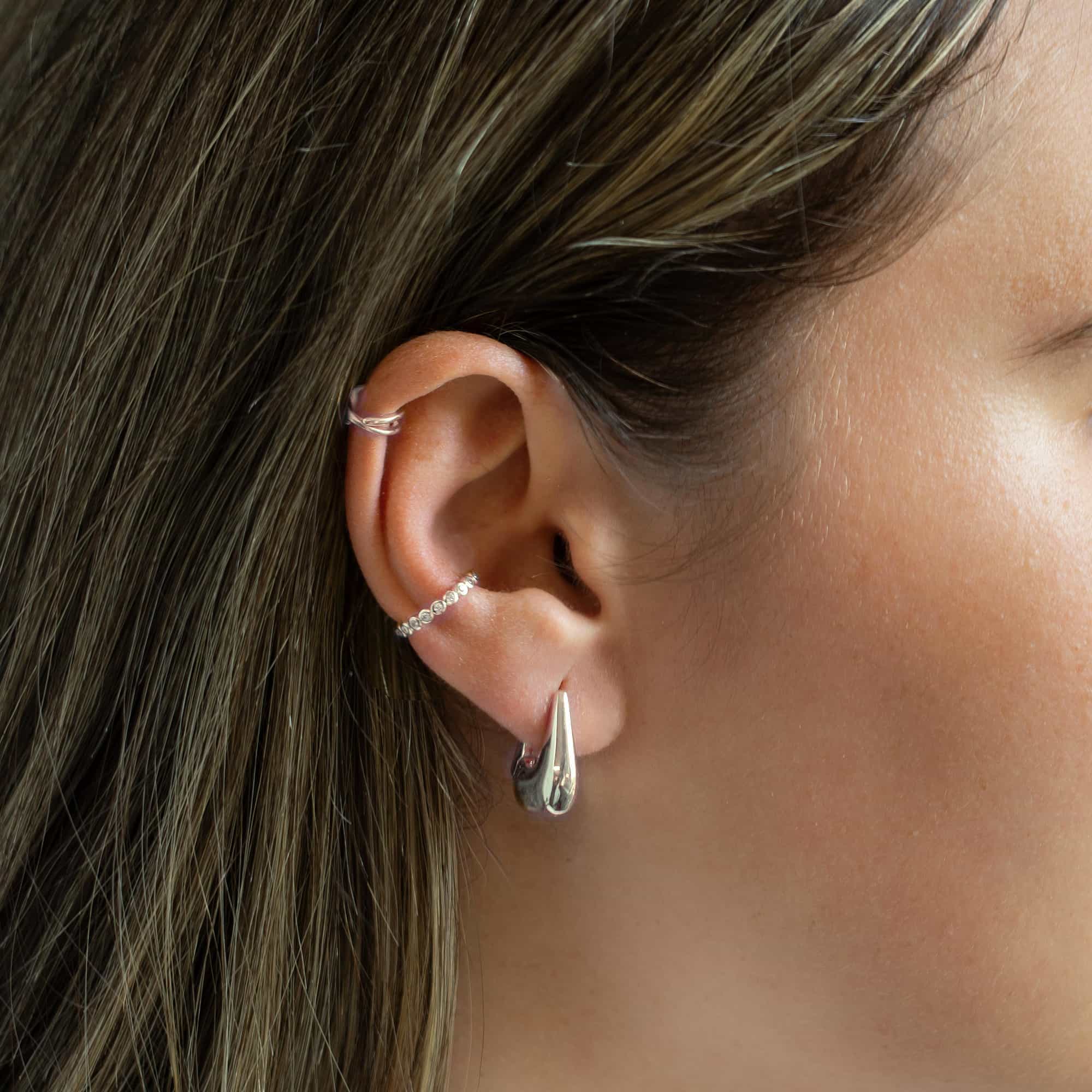 Sterling silver tapered huggie hoop shown on a model's lobe with stacked ear cuffs