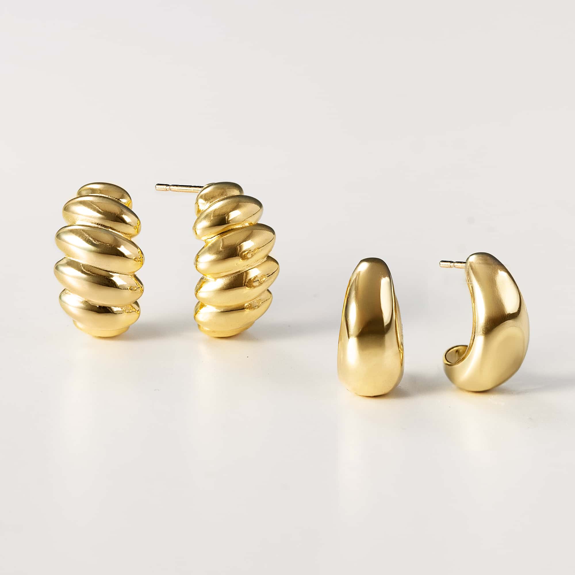 Gold vermeil chunky J-hoop earrings beside a ribbed shrimp-style hoop, on a white background