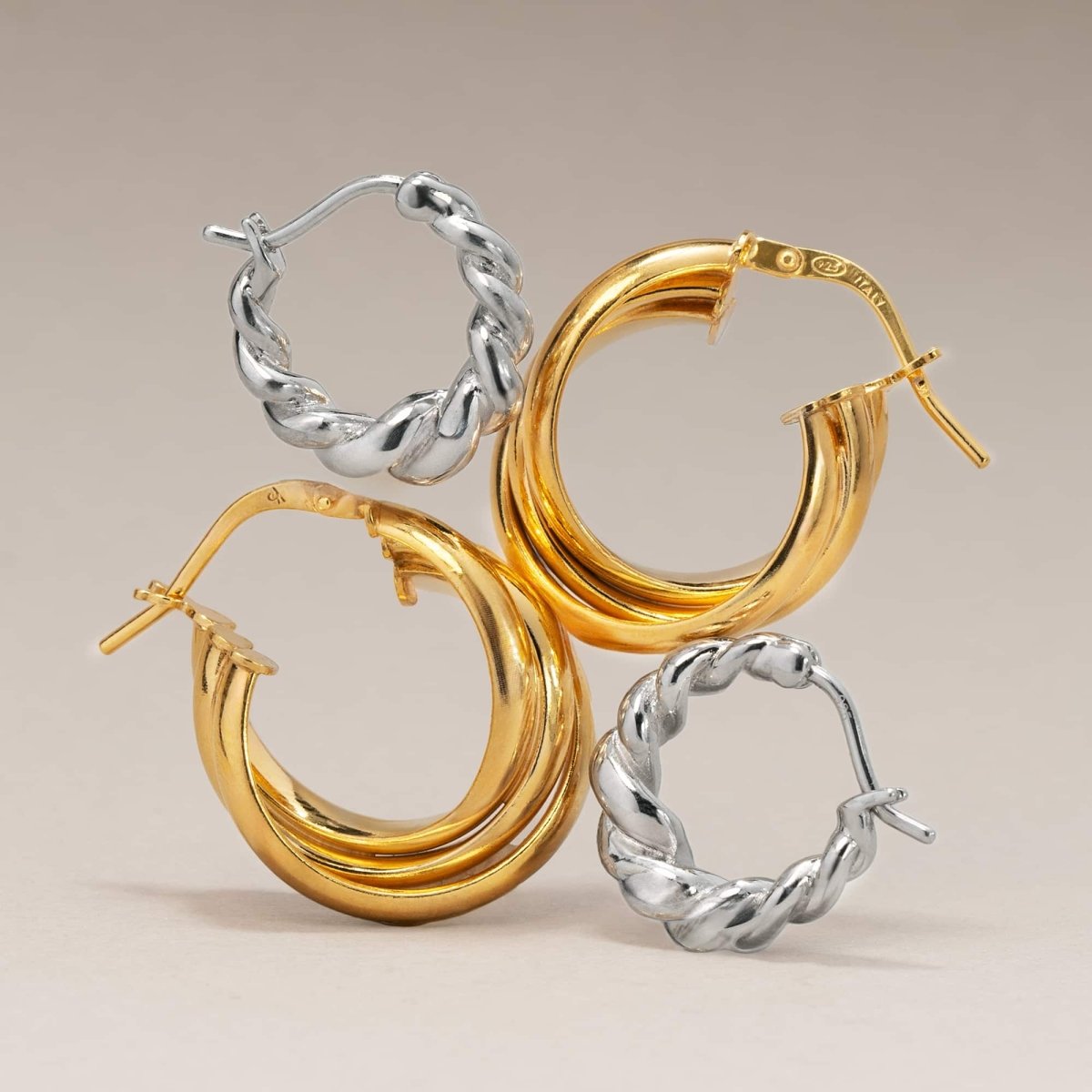 Gold and silver chunky twisted-rope hoop earrings, two pairs arranged on a cream background