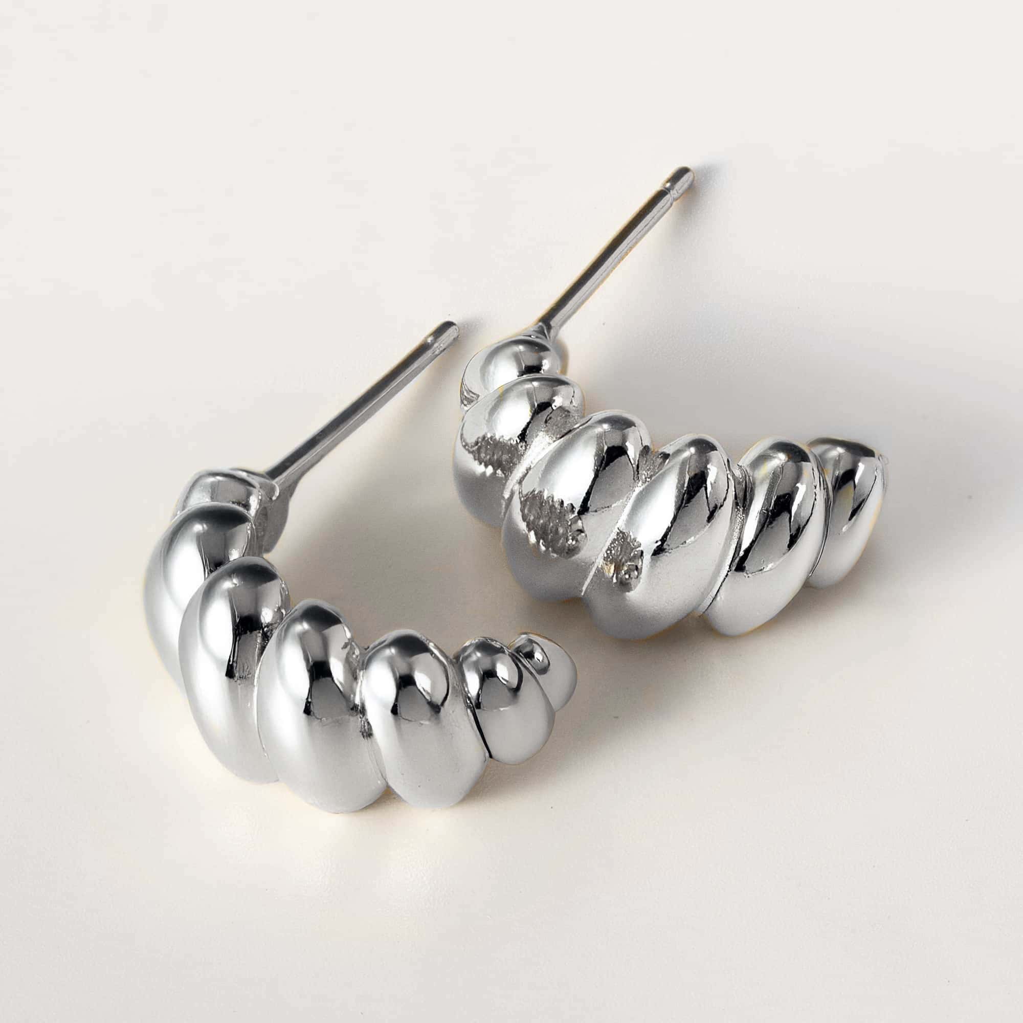 Sterling silver croissant dome stud earrings shown laid on cream with posts visible
