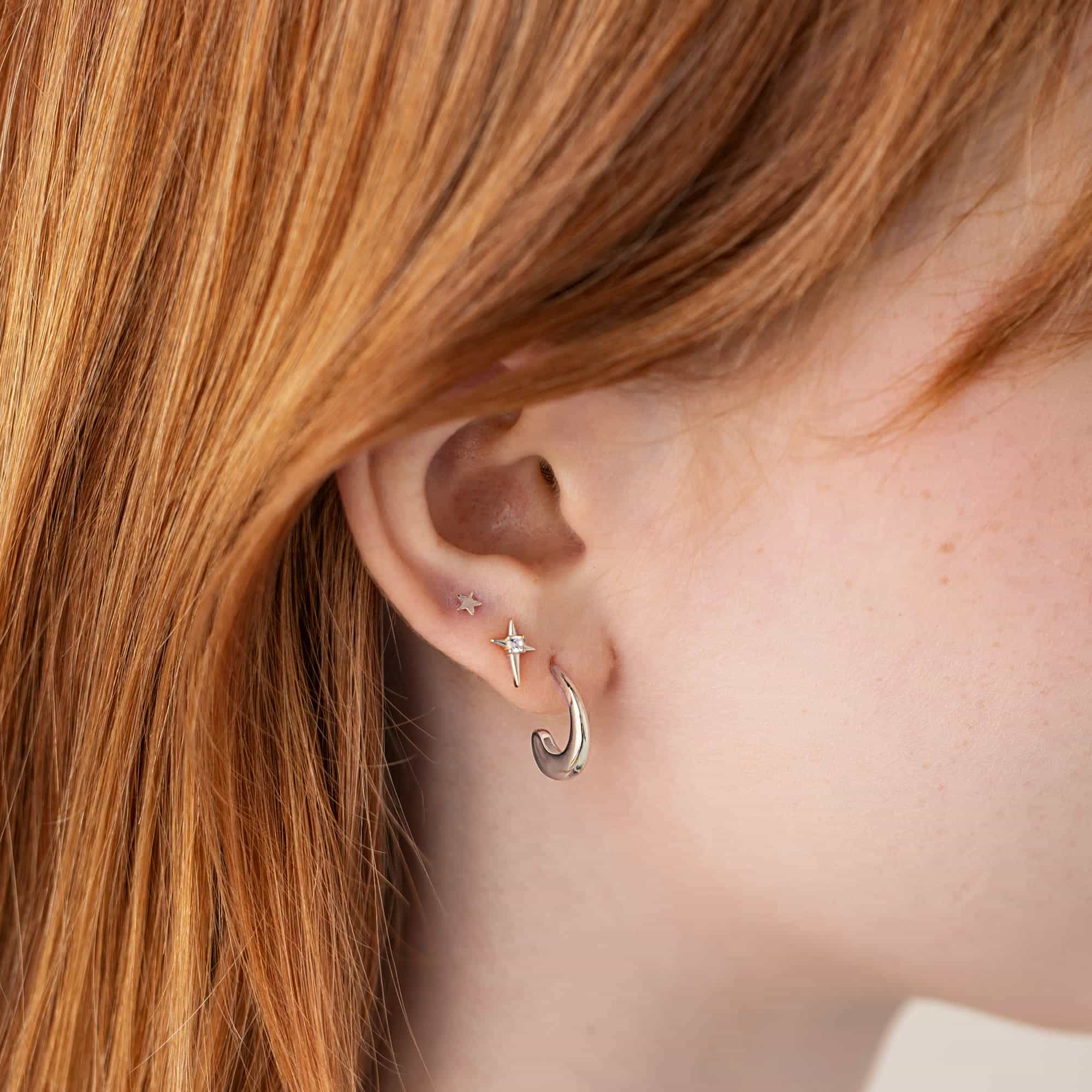 Silver small J-hoop and a tiny star stud with a clear stone, shown on a model's lobe