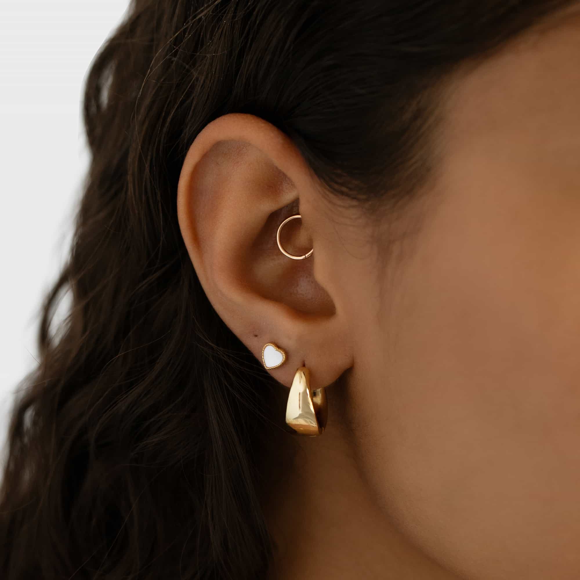 Gold vermeil mini mother of pearl heart stud shown on a model's lobe with hoops and a daith ring
