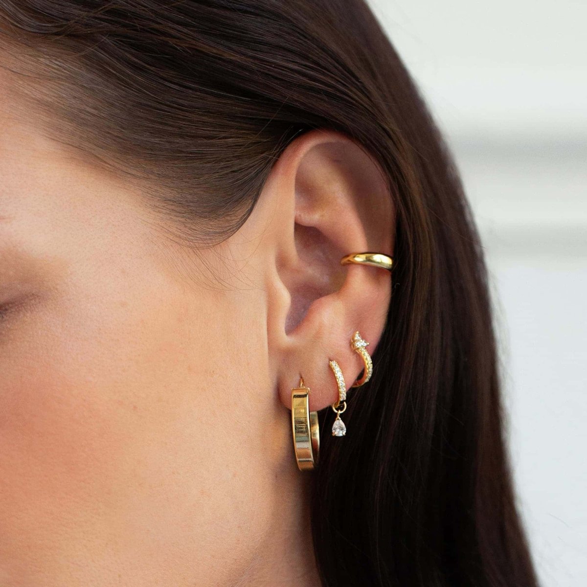 Close-up of woman's ear featuring Gold Vermeil Clover Pave Huggie Earrings, large gold hoop, and cuff. 