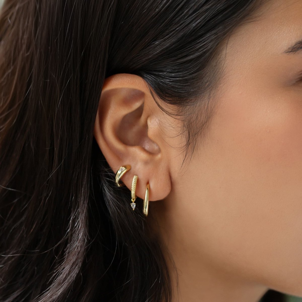 Gold vermeil small J hoop styled in an ear stack with textured huggies and a cuff
