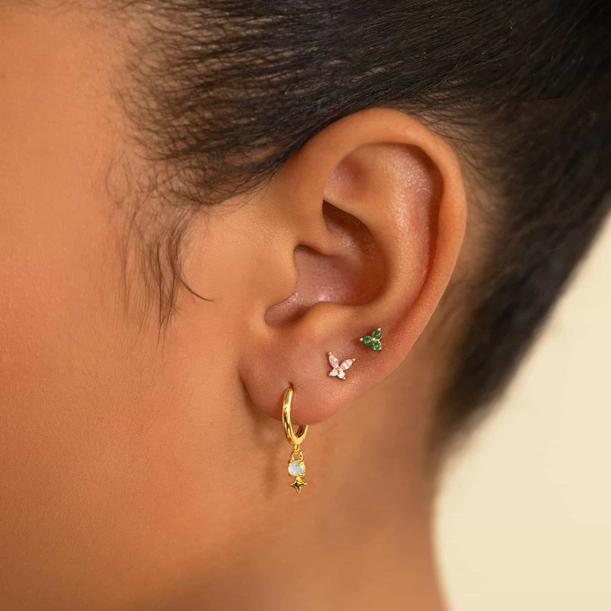 14K gold green clover stud above a hoop with a dangling charm, shown on a model's lobe