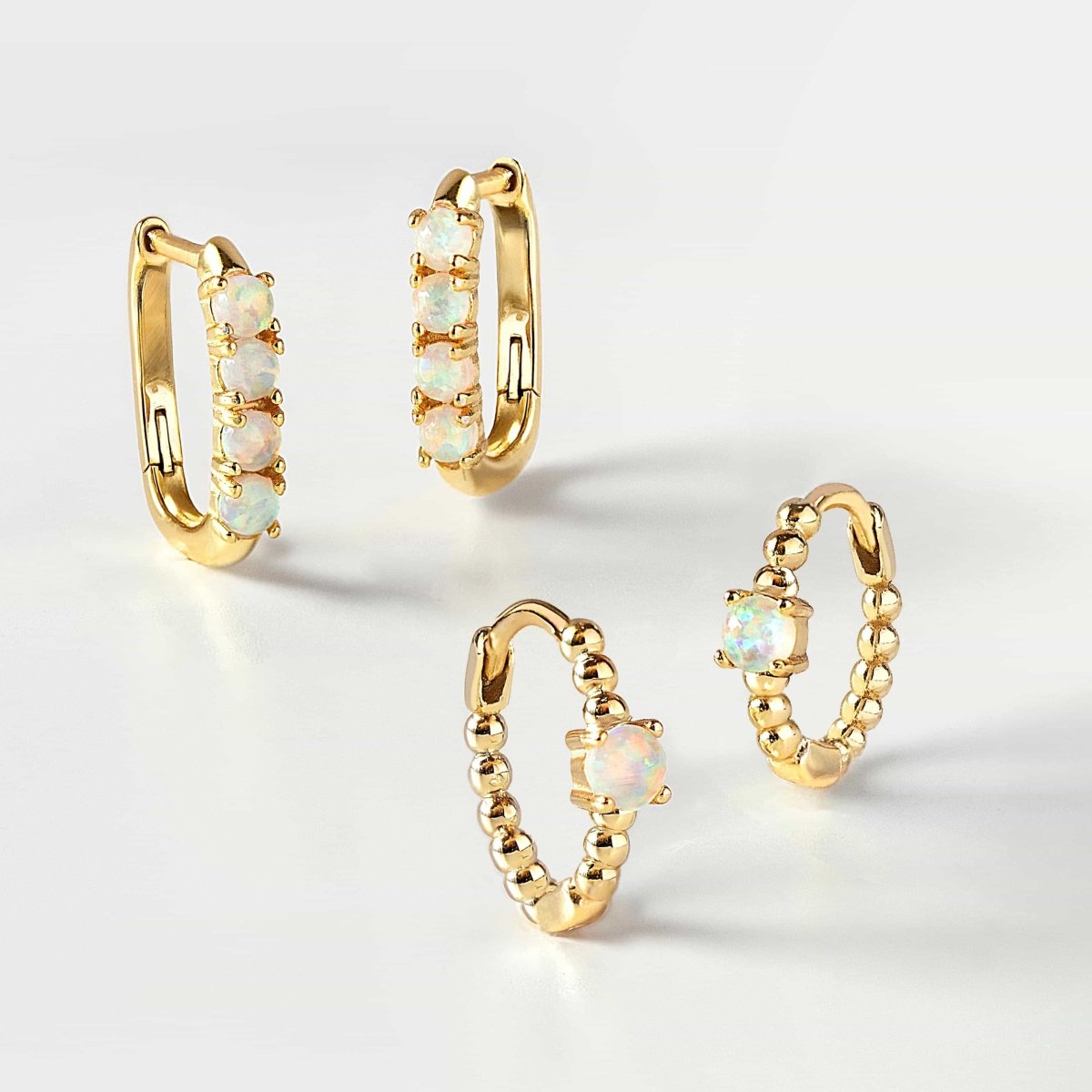 Gold opal huggie hoops in beaded and multi-stone styles grouped on a white background
