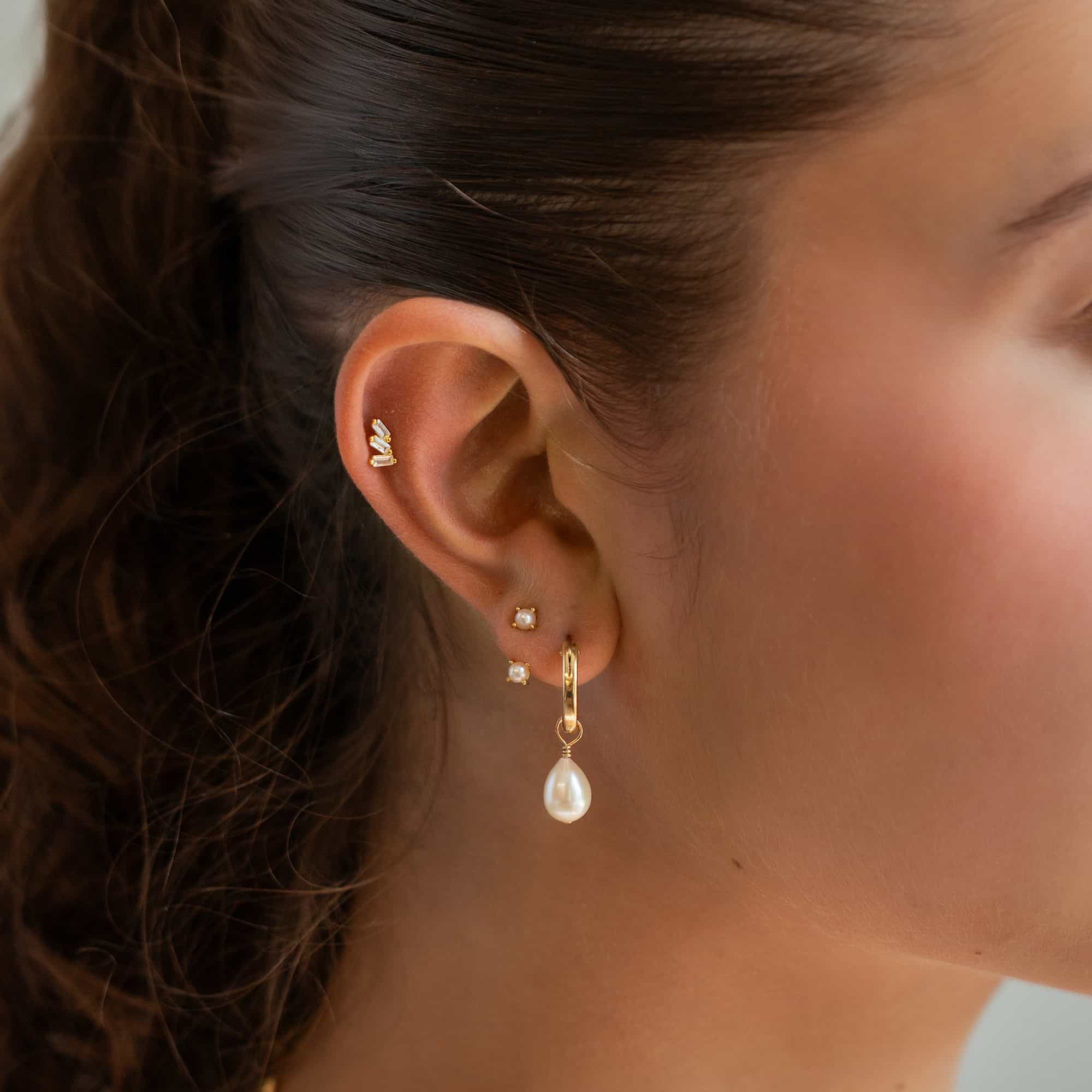 Gold ear stack with baguette studs, pearl studs and a teardrop pearl hoop, shown on a model's ear
