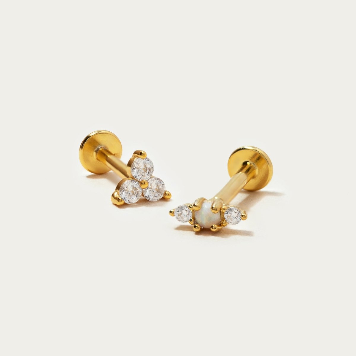 Gold vermeil trio flat back studs, one trinity and one white opal with clear stones, on a cream background