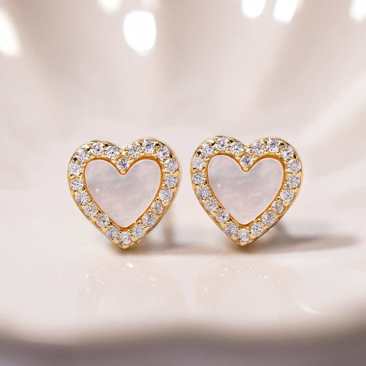 Gold vermeil mother of pearl heart studs with a clear stone halo, close-up detail on a cream background