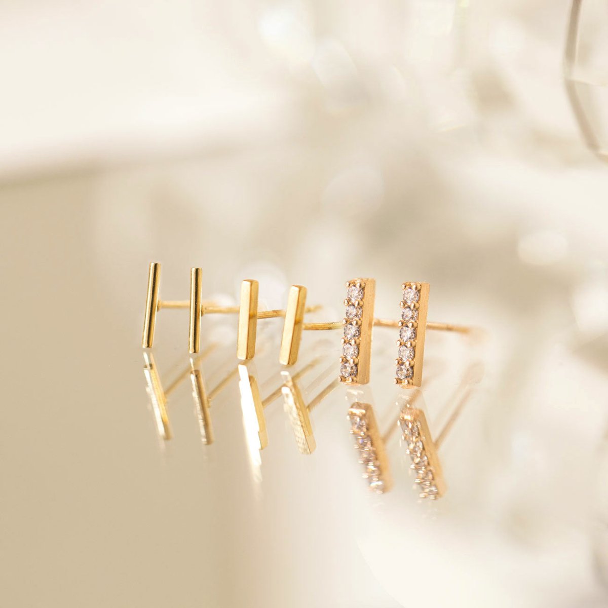 Gold vermeil bar studs, plain and pave with clear stones, close-up detail on a soft surface