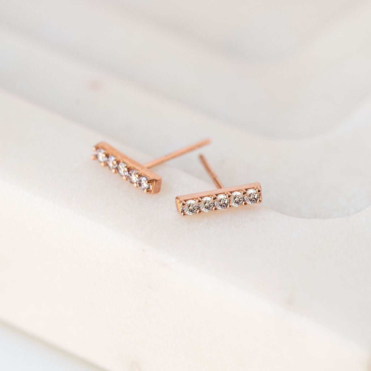 Rose gold vermeil pave bar stud earrings with clear stones, angled close-up on cream marble
