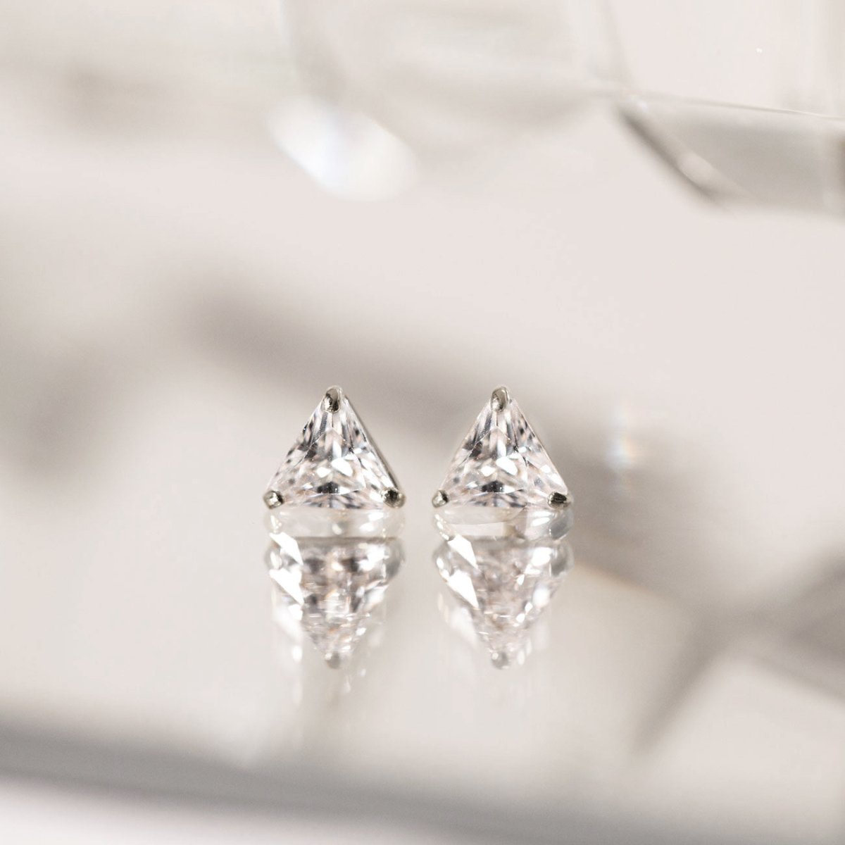 14K white gold triangle white zirconia studs, close-up detail on a reflective surface