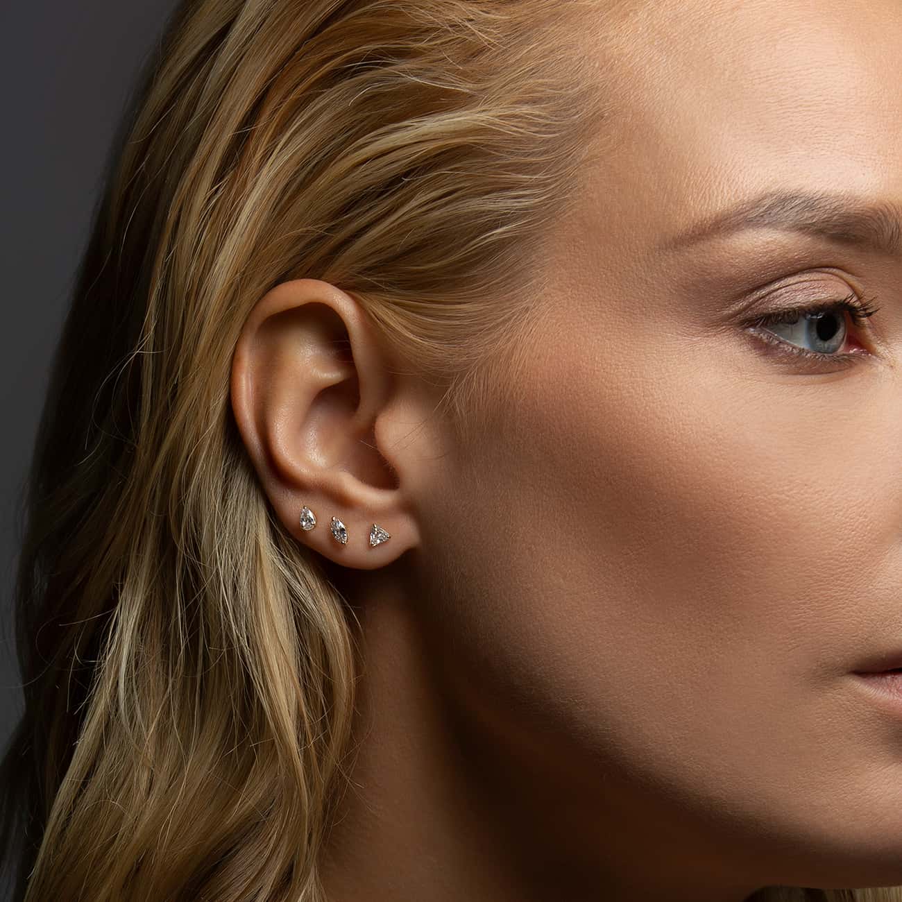 Row of three small gold clear-stone studs styled in a lobe stack, shown on a model's ear