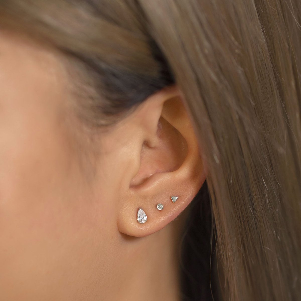 14K white gold tiny pear stud with two small clear-stone studs on a model's lobe