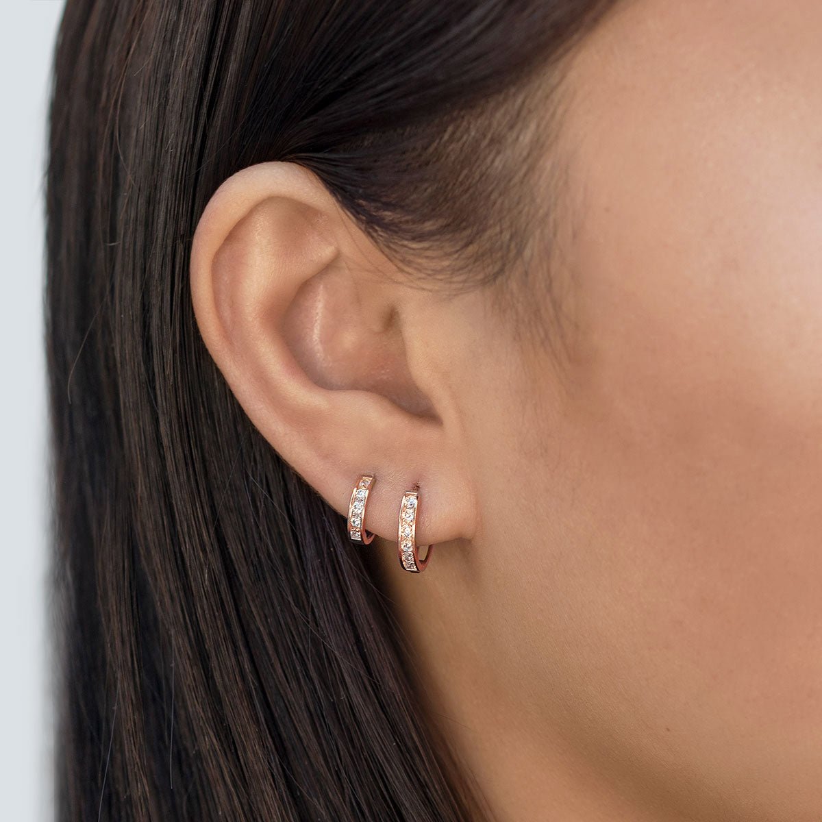 Rose gold vermeil huggie hoops with round clear cubic zirconia shown on a model's earlobe