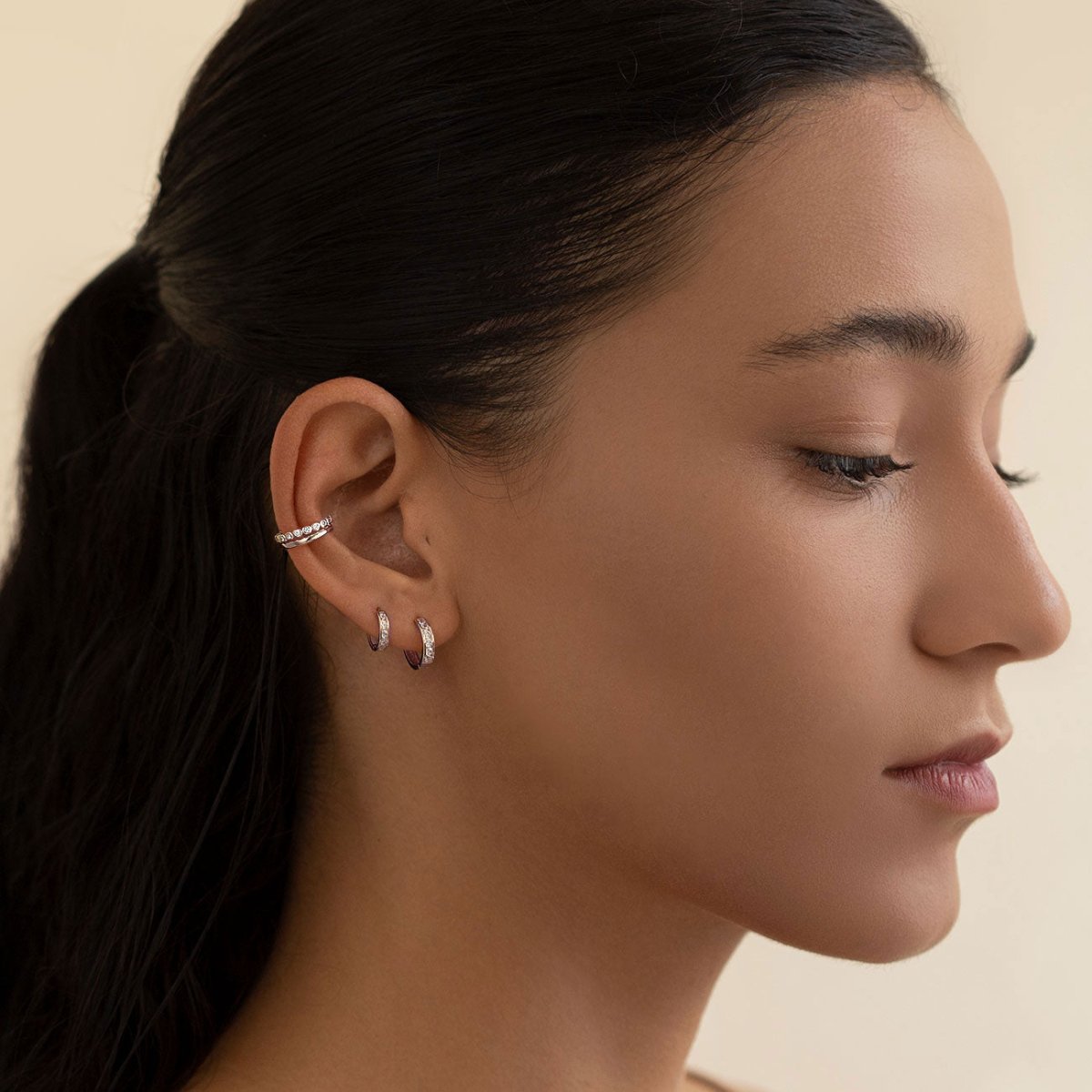 Sterling silver huggie hoops with round clear cubic zirconia shown on a model's ear