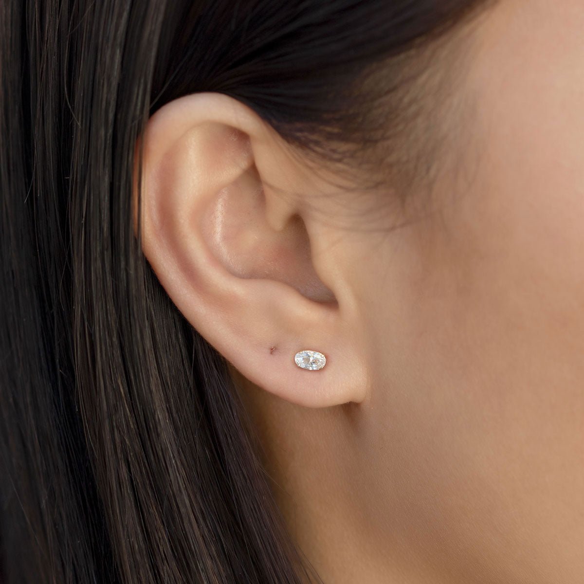 14K gold oval white zirconia stud earring shown on a model's lobe