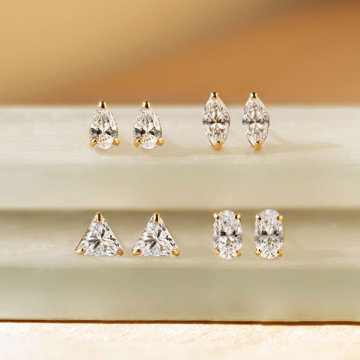 14K gold studs in pear, marquise, trillion and oval white zirconia shapes, on a pale ledge