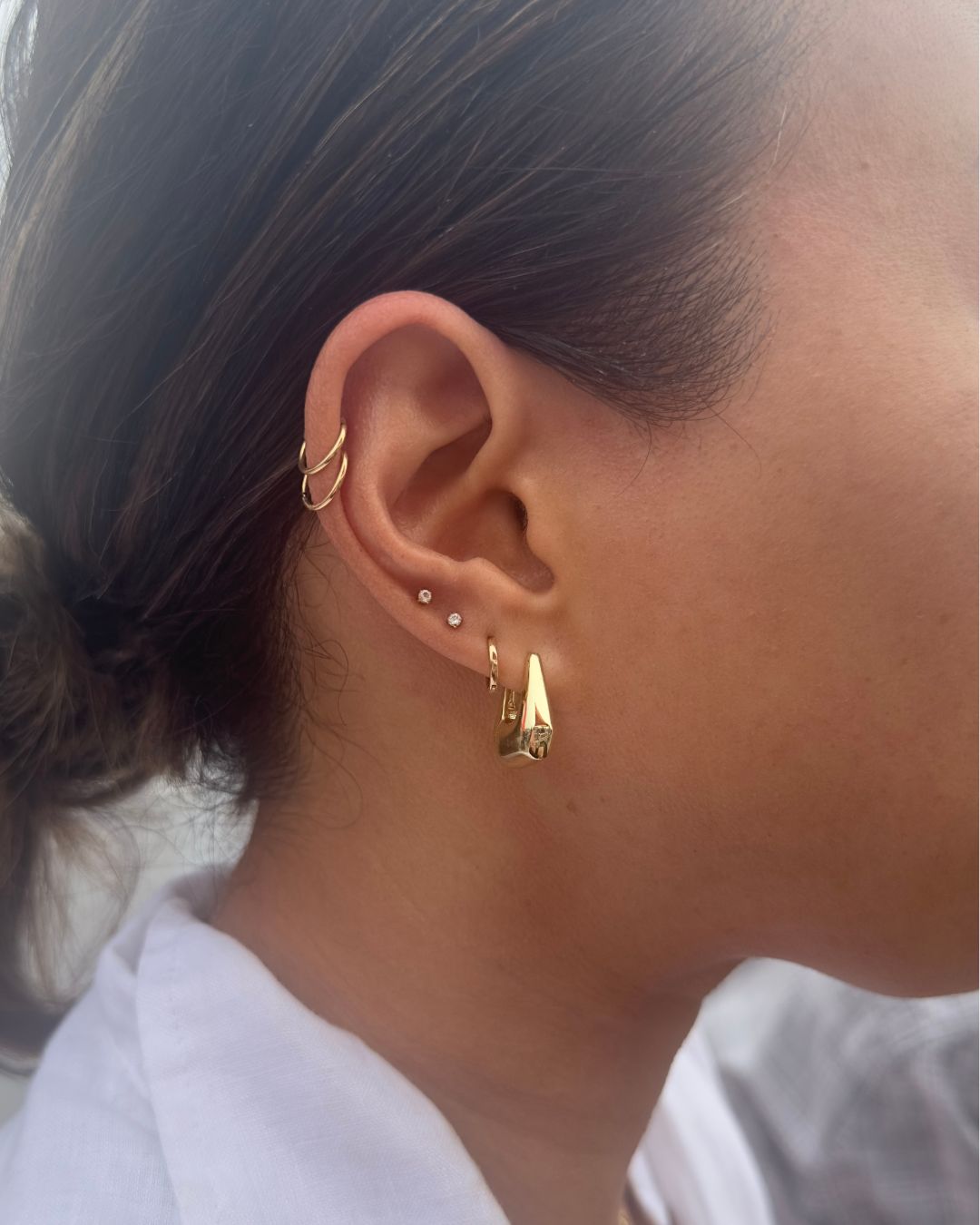 Ear worn with a chunky tapered gold hoop, small huggie hoop, two crystal studs and a double gold ear cuff