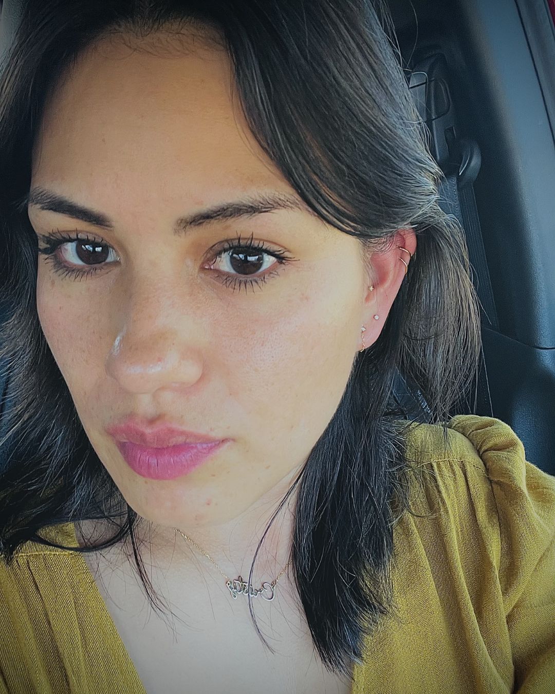 Close-up selfie showing a gold script name necklace, a helix hoop and small gold ear studs