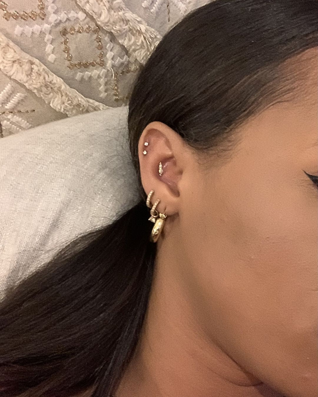Close-up of an ear stacked with gold hoops, a chunky lobe hoop, and small crystal studs in the upper cartilage