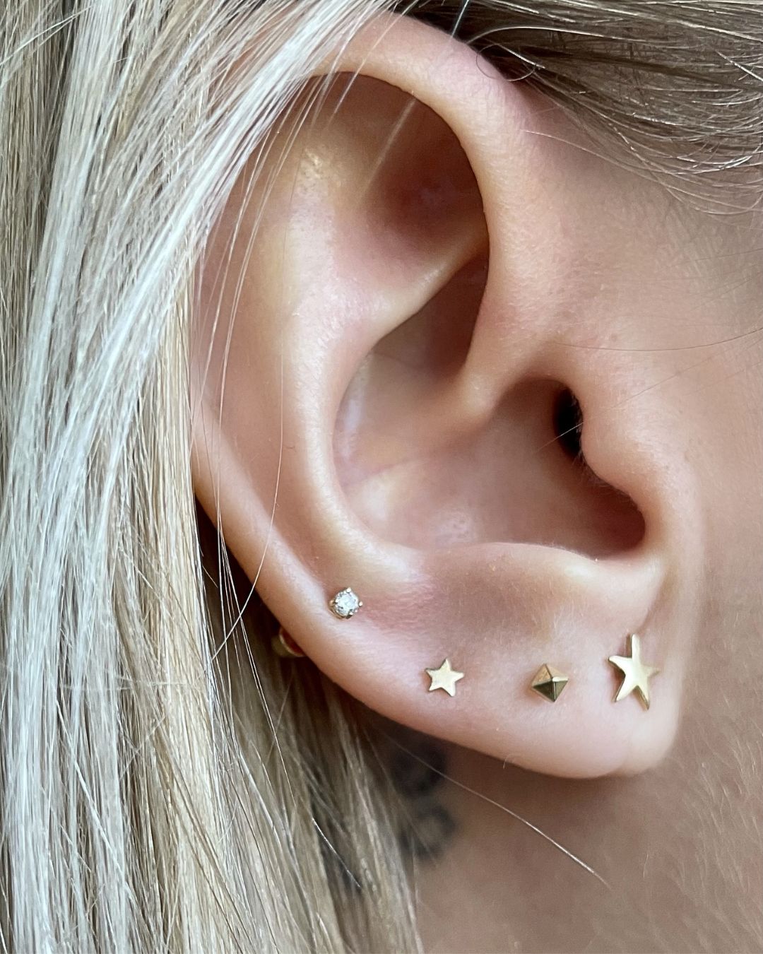 Close-up of an ear wearing four gold lobe studs: a small crystal, two stars and a faceted square