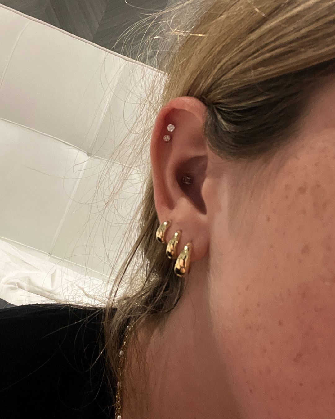 Ear worn with three gold huggie hoops along the lobe and two small crystal studs in the upper ear