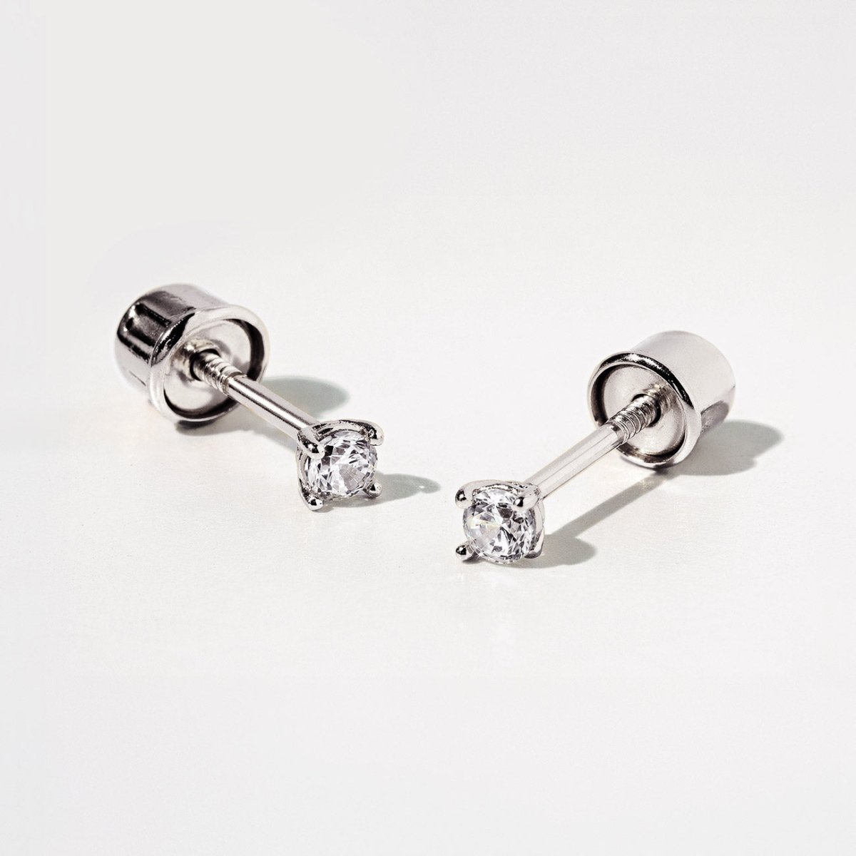 Pair of 14K white gold screw-back solitaire studs with round clear white sapphires, on a white background
