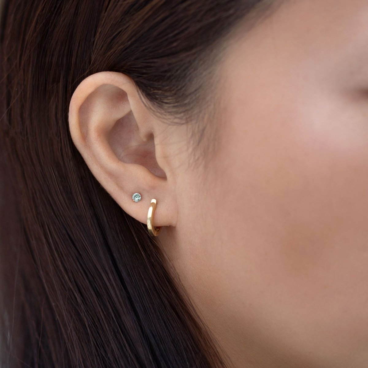 14K white gold aquamarine tiny stud with a pale-blue stone, shown on a model's lobe