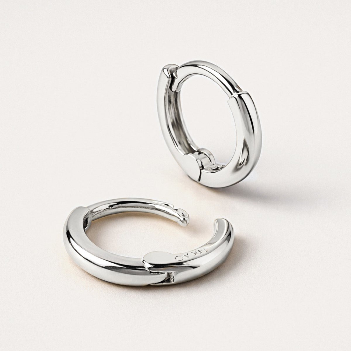 14K white gold mini huggie hoops close-up detail showing the smooth band and hinge, on a cream background
