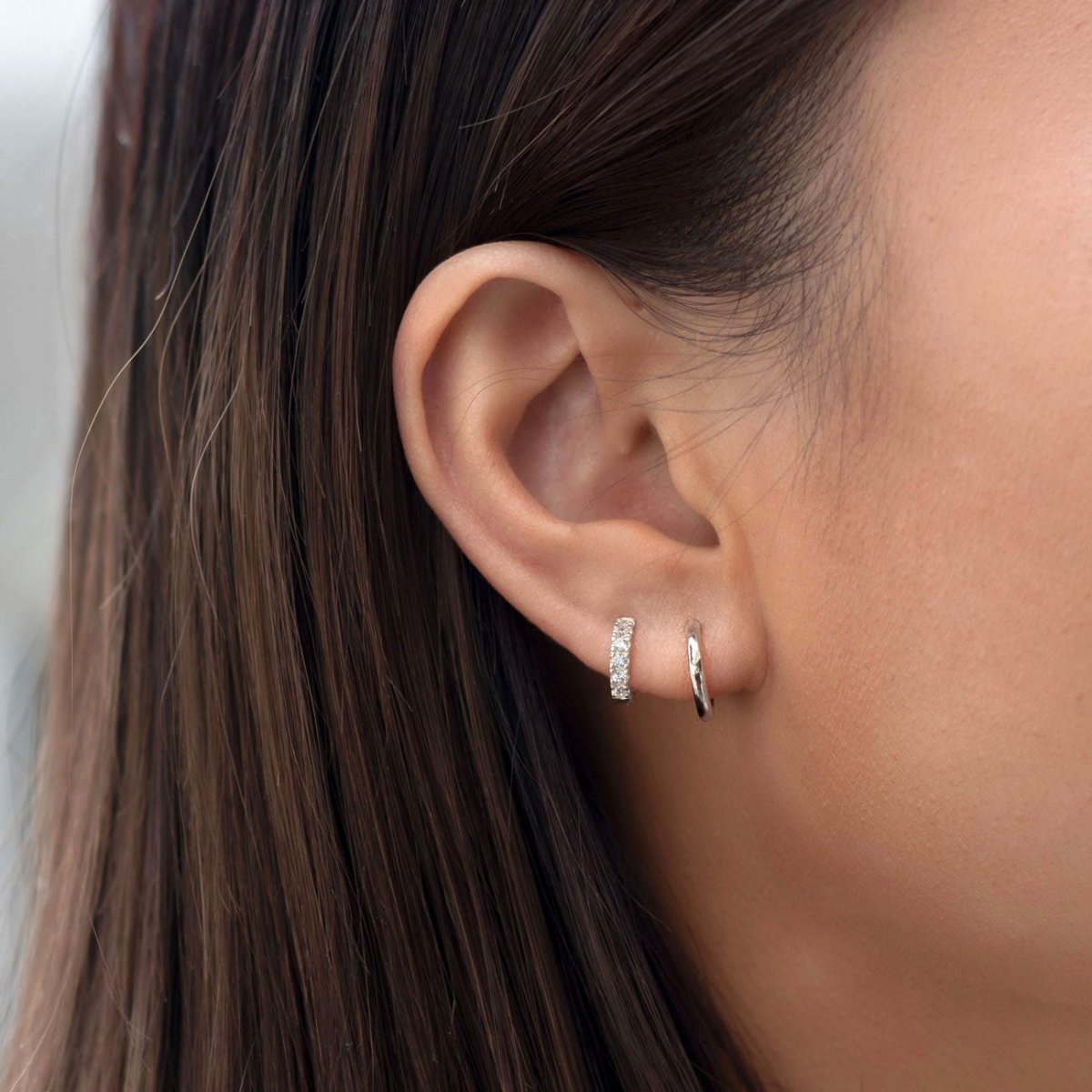 Close-up of woman's ear featuring 14k white gold pave huggie earring and sterling silver midi hoop