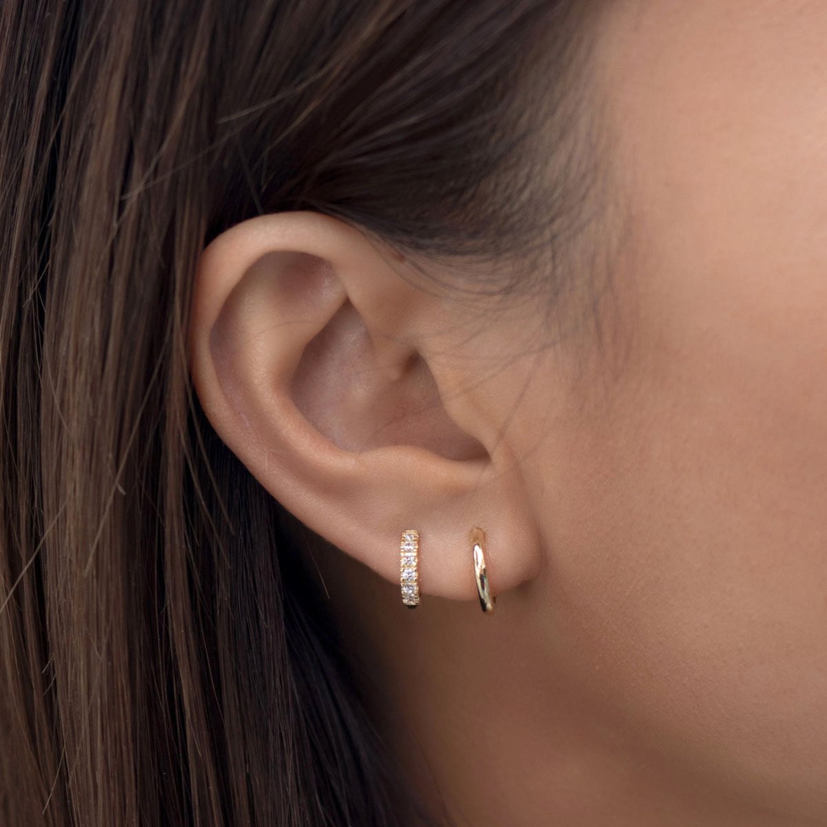 Close-up of woman's ear featuring 14k gold pave huggie earring and 14k gold midi hoop