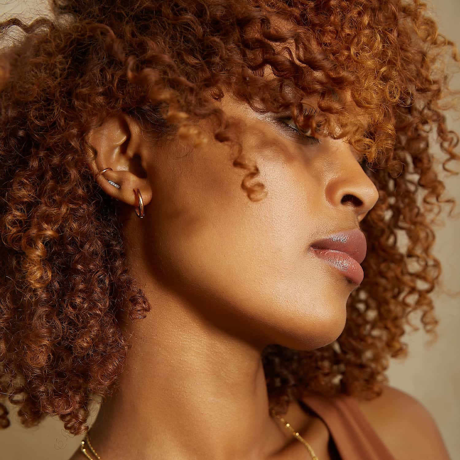 Woman wearing rose gold mini hoops in 14k, rose gold diamond bar studs, and rose gold eternity ear cuff