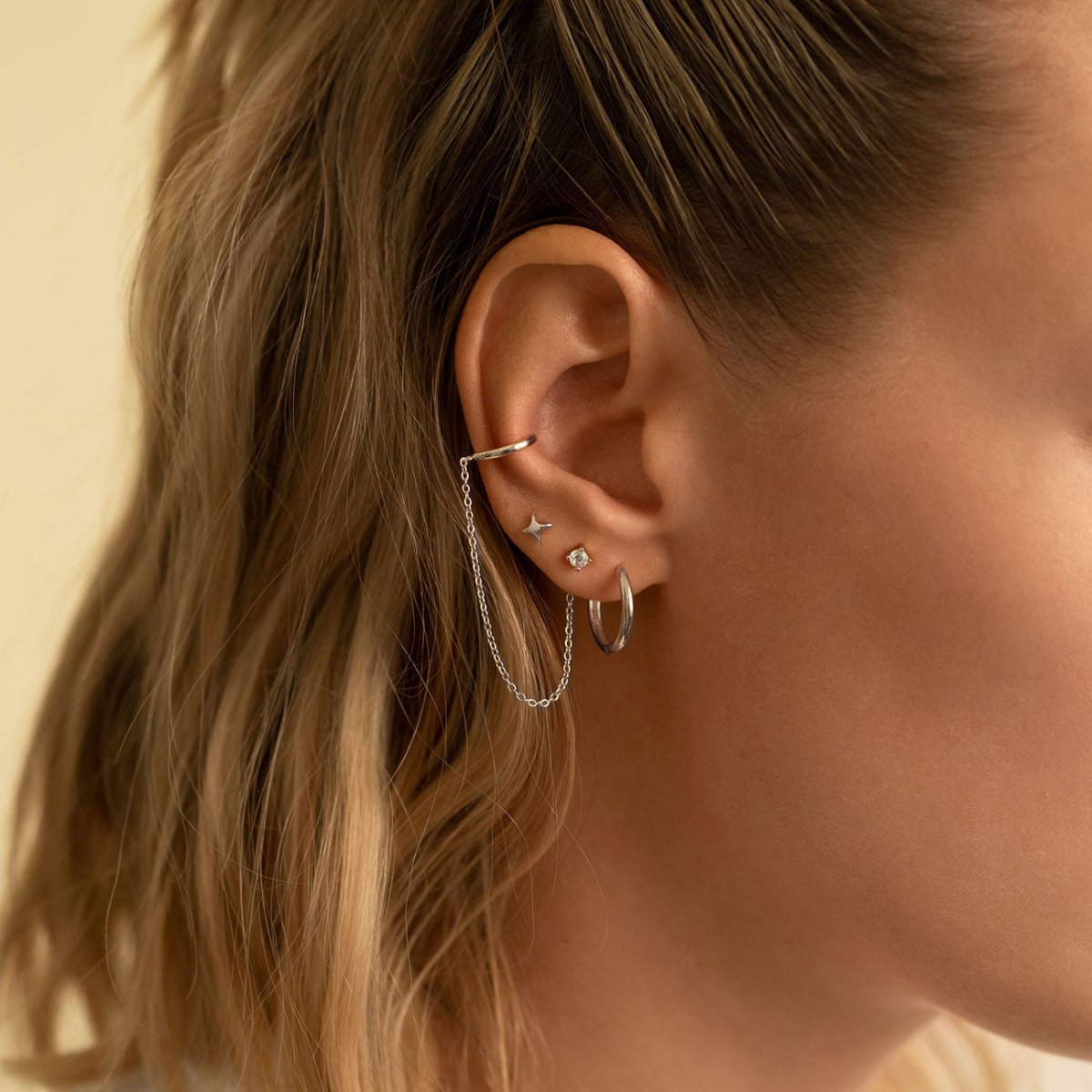 14K white gold four-point star stud in an ear stack with hoops and a chained cuff