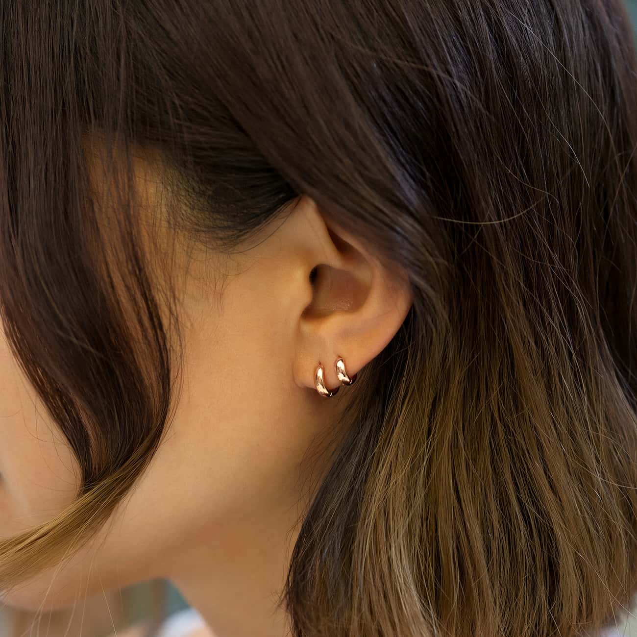 14K rose gold huggie hoops stacked in two lobe piercings, shown on a model's ear