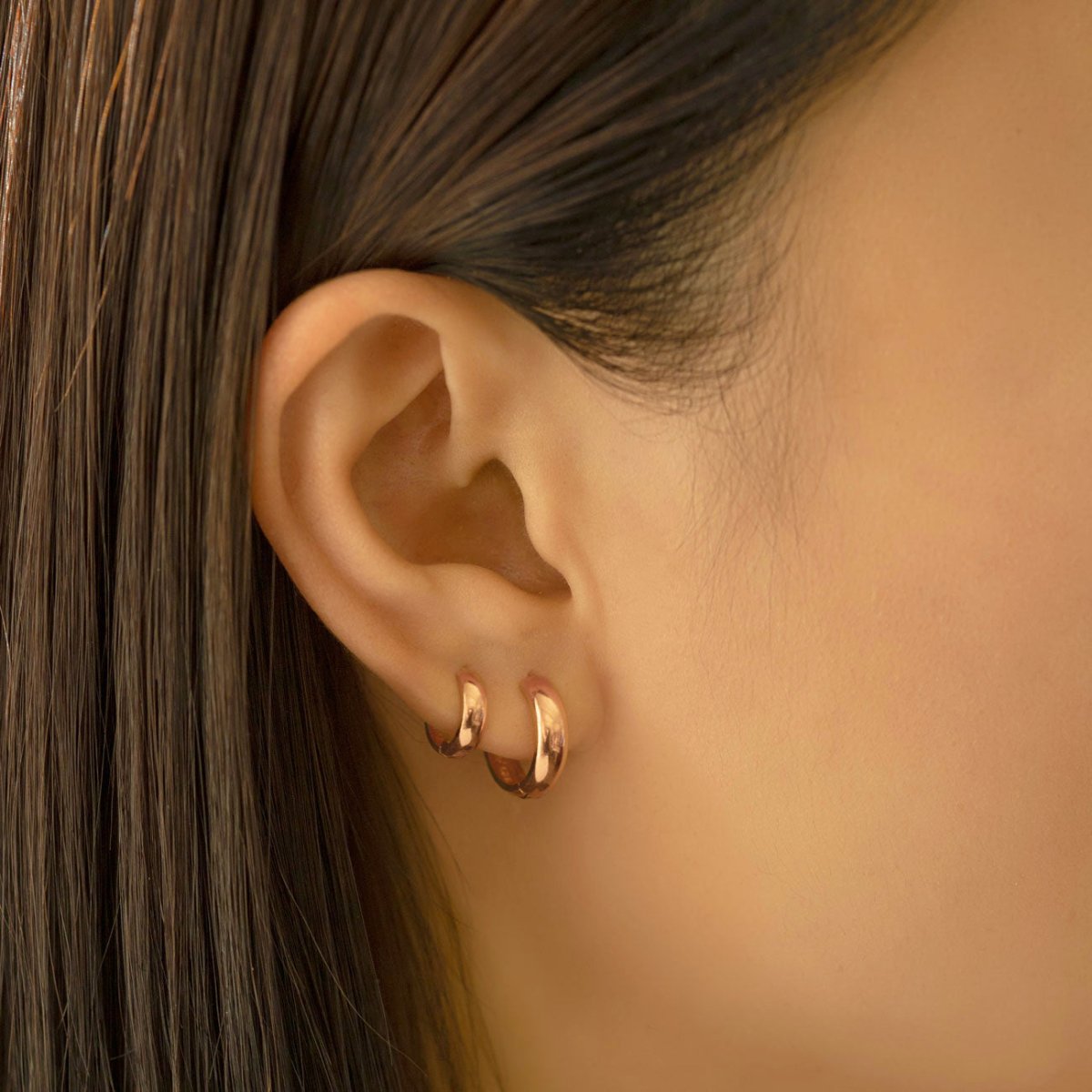 Close-up of woman's ear featuring 14k rose gold boyfriend huggie and rose gold mini hoops