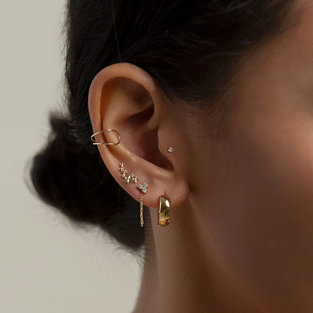 14K gold flat back zirconia stud shown on a model's ear among a stacked curated lobe and helix set