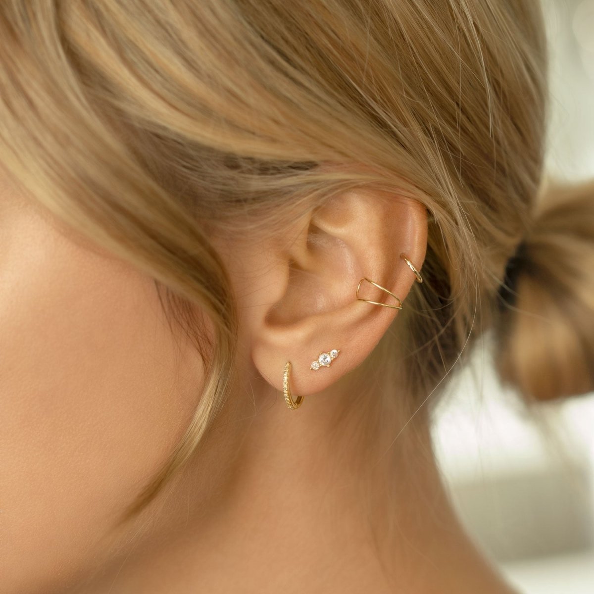Close up of woman's ear featuring 14K Solid Gold Trio Bar Pave Studs, gold hoop earring, and ear cuff