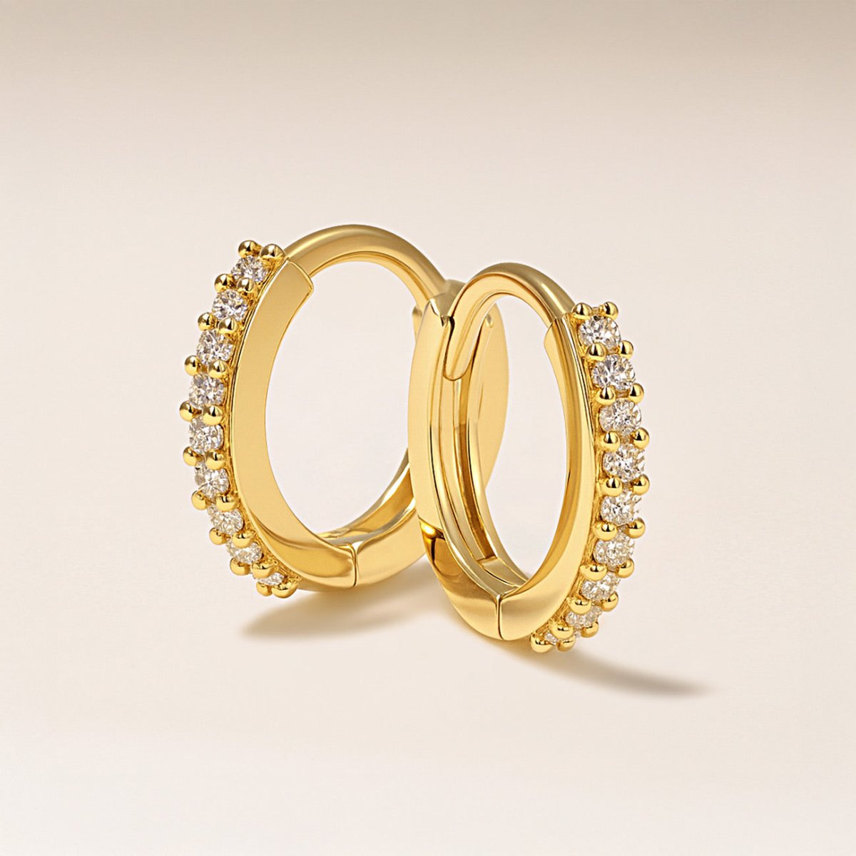 14K gold pavé huggie hoops set with moissanite, angled to show the hinged closure, on a cream background