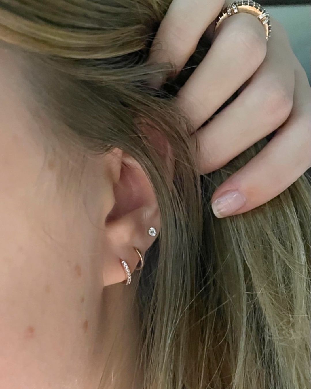 Ear with hair held back, showing a crystal-set gold hoop, a plain gold hoop and a crystal stud