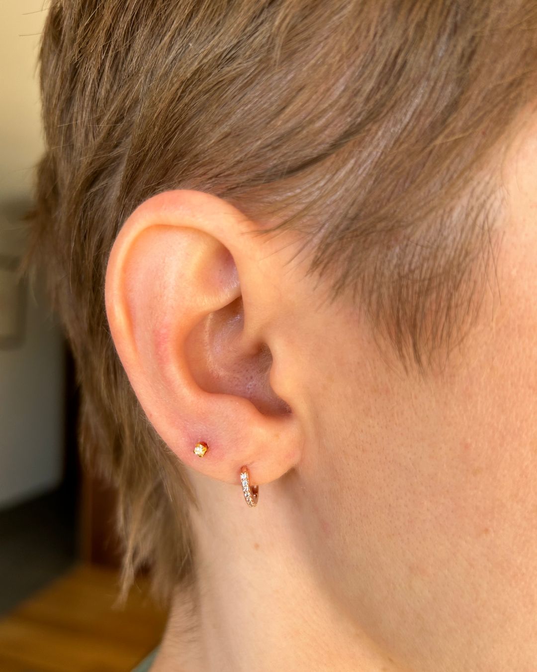 Ear worn with a small gold stone stud in the lobe and a crystal-set gold huggie hoop in a second lobe piercing