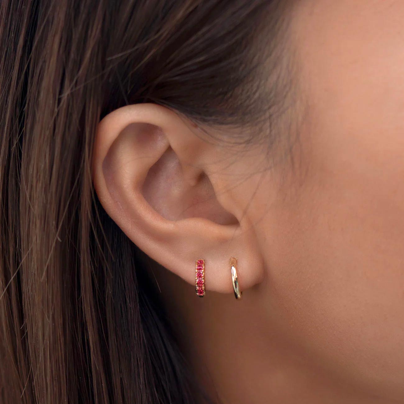 Close-up of woman's ear featuring 14K Gold Gemstone Pavé Huggies Ruby and 14K Gold Pavé Huggies. 