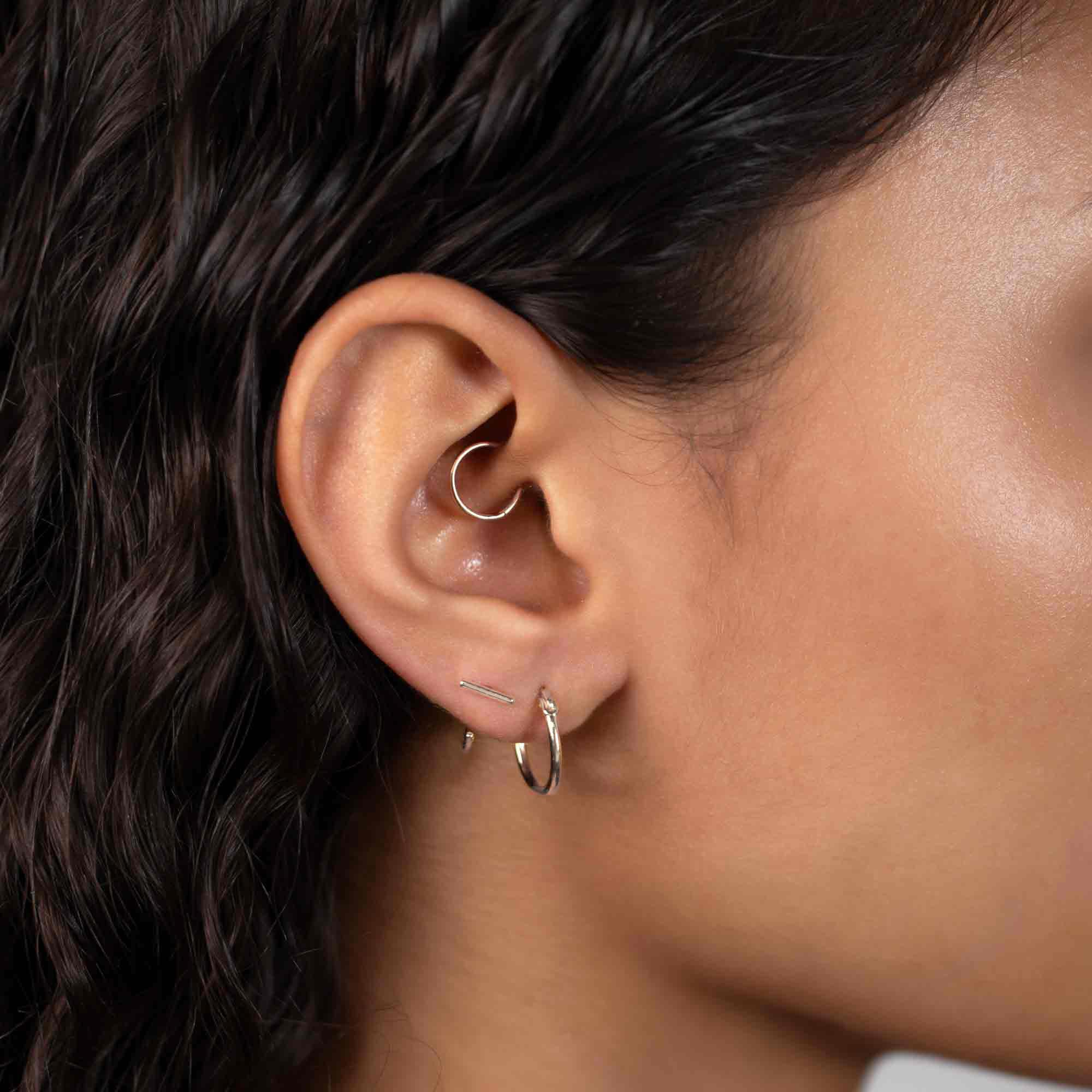 Sterling silver bar huggie earrings styled in a multi-piercing ear stack on a model